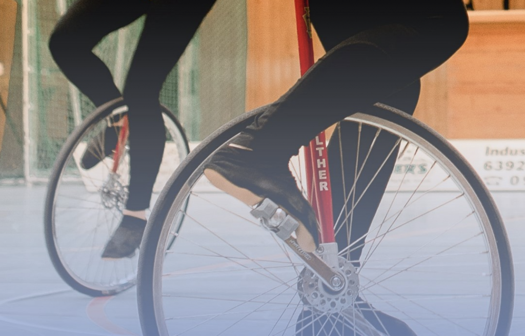 Das Bild zeigt zwei Einradfahrer mit Beinen und Rädern in einer Halle
